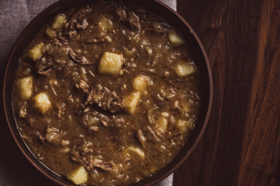 Austrian Goulasch flatlay image. The goulasch is in a brown bowl that is on top of a dark brown wooden surface.